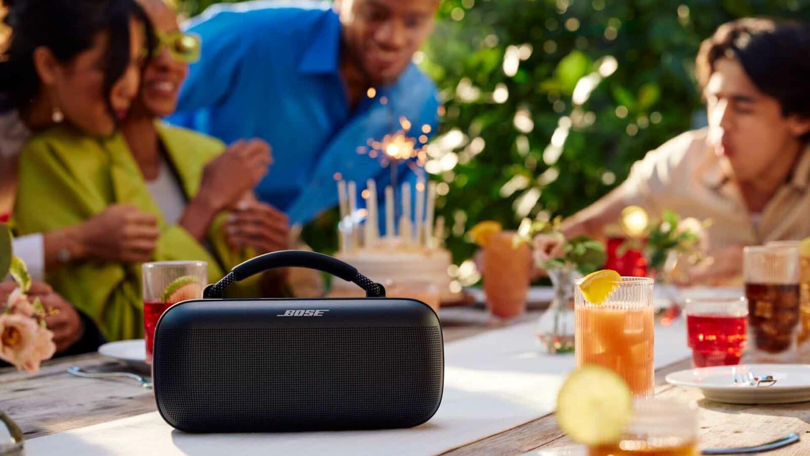 Friends celebrating with Bose speaker on table.