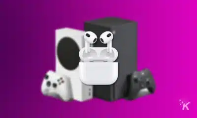 render of airpods 3 with case floating in front of two xbox consoles on a purple background