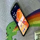 android smartphone on a deskmat with a dinosaur barfing a rainbow on it