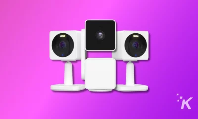 Three white security cameras with dark lenses are symmetrically arranged against a gradient purple background, depicting a modern home surveillance system setup.