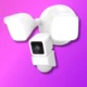 The image shows a modern white security camera system with multiple motion sensors on a vibrant purple background, representing smart home technology.