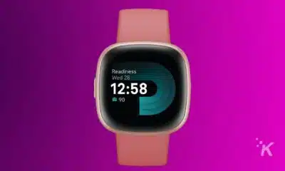 A smartwatch with a peach strap displays the time 12:58 and a readiness score of 90 on its screen against a purple background.