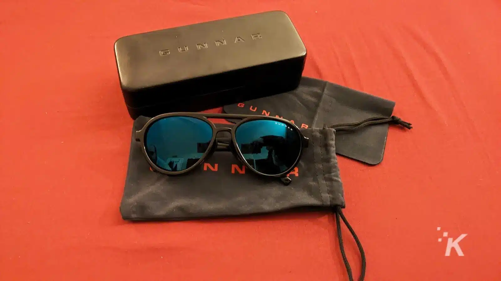 Gunnar sunglasses with case on red surface.