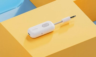 A white wireless twelve south headphone adapter with a plus and minus button lies on a dual-shade yellow background, with text "AirFly" printed on its side.
