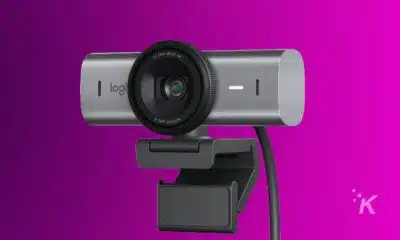 A Logitech 4K ultra-wide MX Brio 705 webcam with an 8.5MP sensor, mounted on a monitor clip, against a purple background.