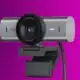 A Logitech 4K ultra-wide MX Brio 705 webcam with an 8.5MP sensor, mounted on a monitor clip, against a purple background.