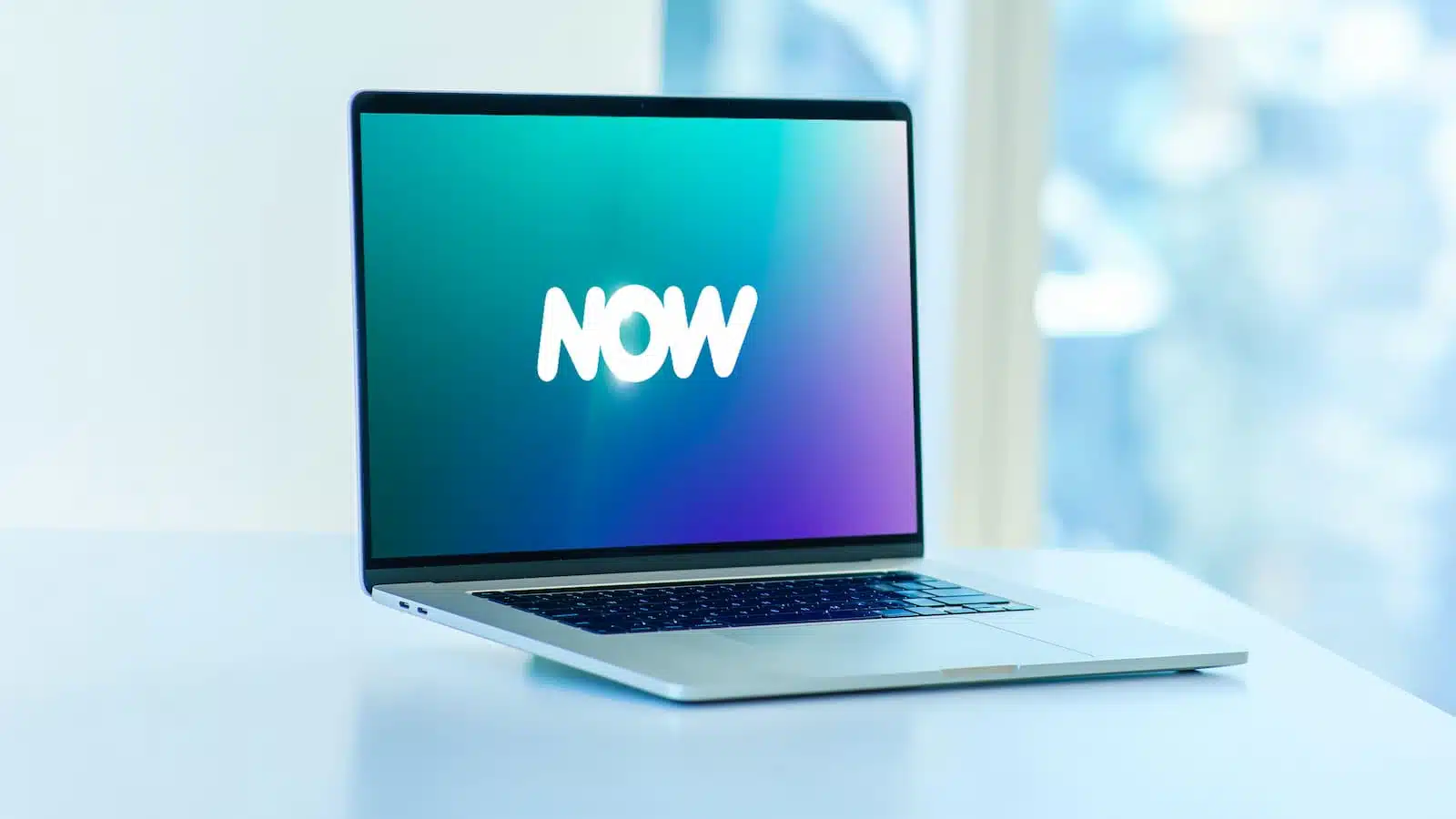 Laptop on desk displaying "NOW" on screen