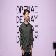 An individual is standing on stage with "OPENAI DEMO DAY" in the background, wearing a dark green sweater and dark pants, presenting to an audience.
