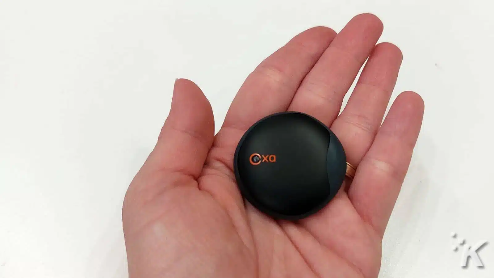 Hand holding small black wireless device with logo.