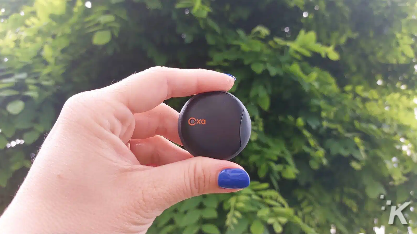 Hand holding a black circular device outdoors.