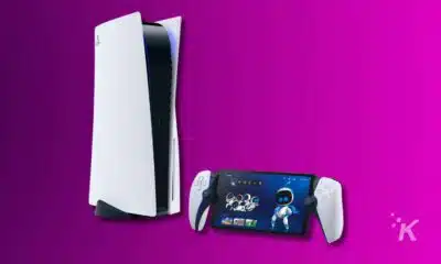 The image features a PlayStation 5 console, its controller, and a handheld device showing a game screen, all against a vivid purple background.