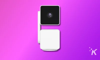 A white smart home camera with block design on a vibrant purple background, with a shadow indicating elevation, minimalistic and modern appearance.