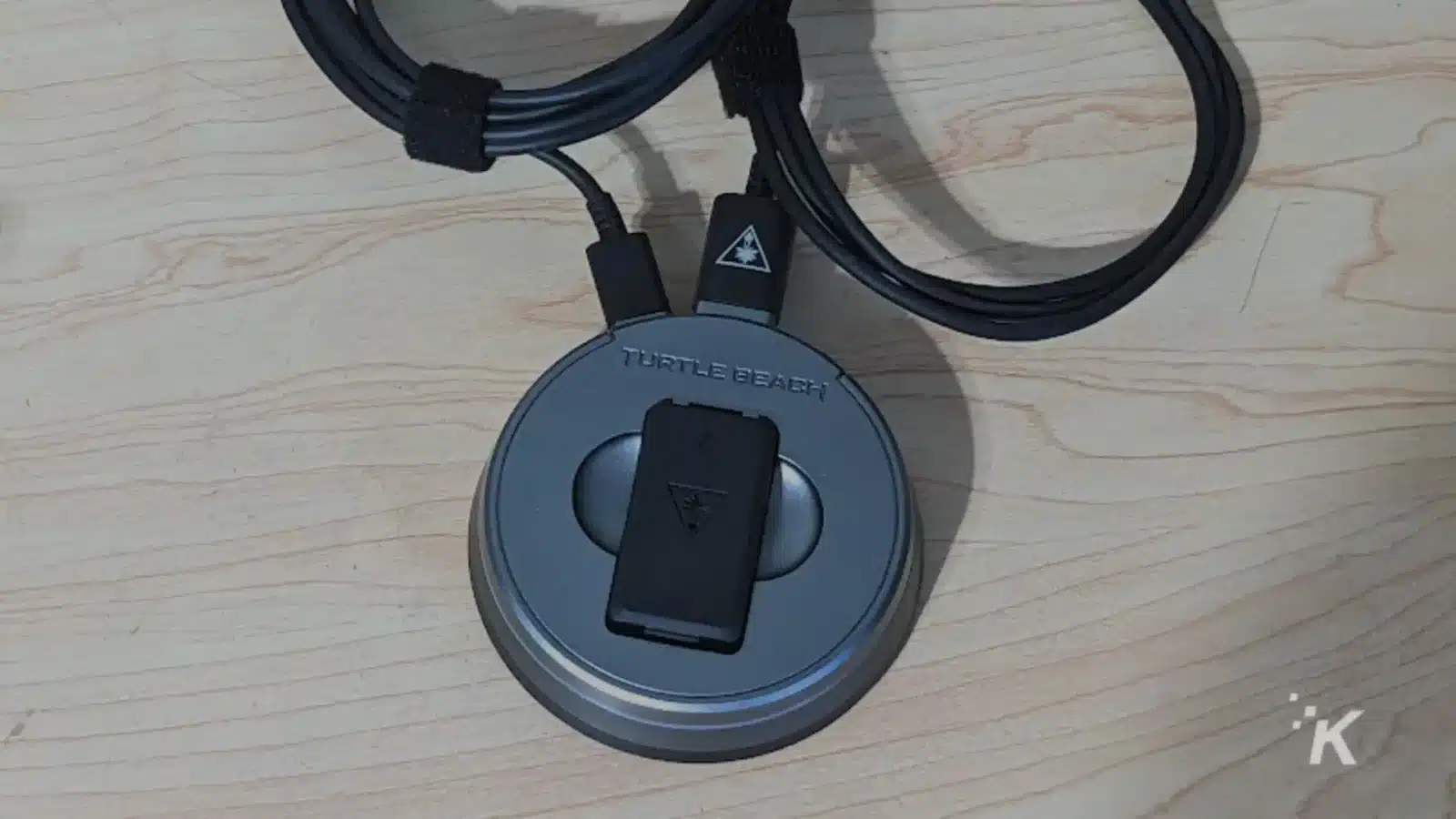 A peripheral electronic device with Turtle Beach K headphones is connected to a gadget via a cable in an indoor setting.