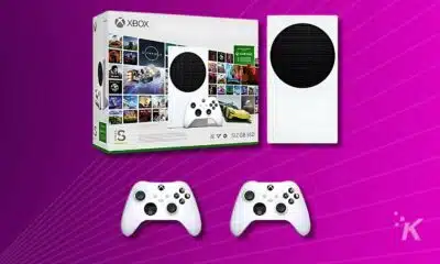 An Xbox Series S gaming console with its packaging box and two wireless controllers on a purple background.