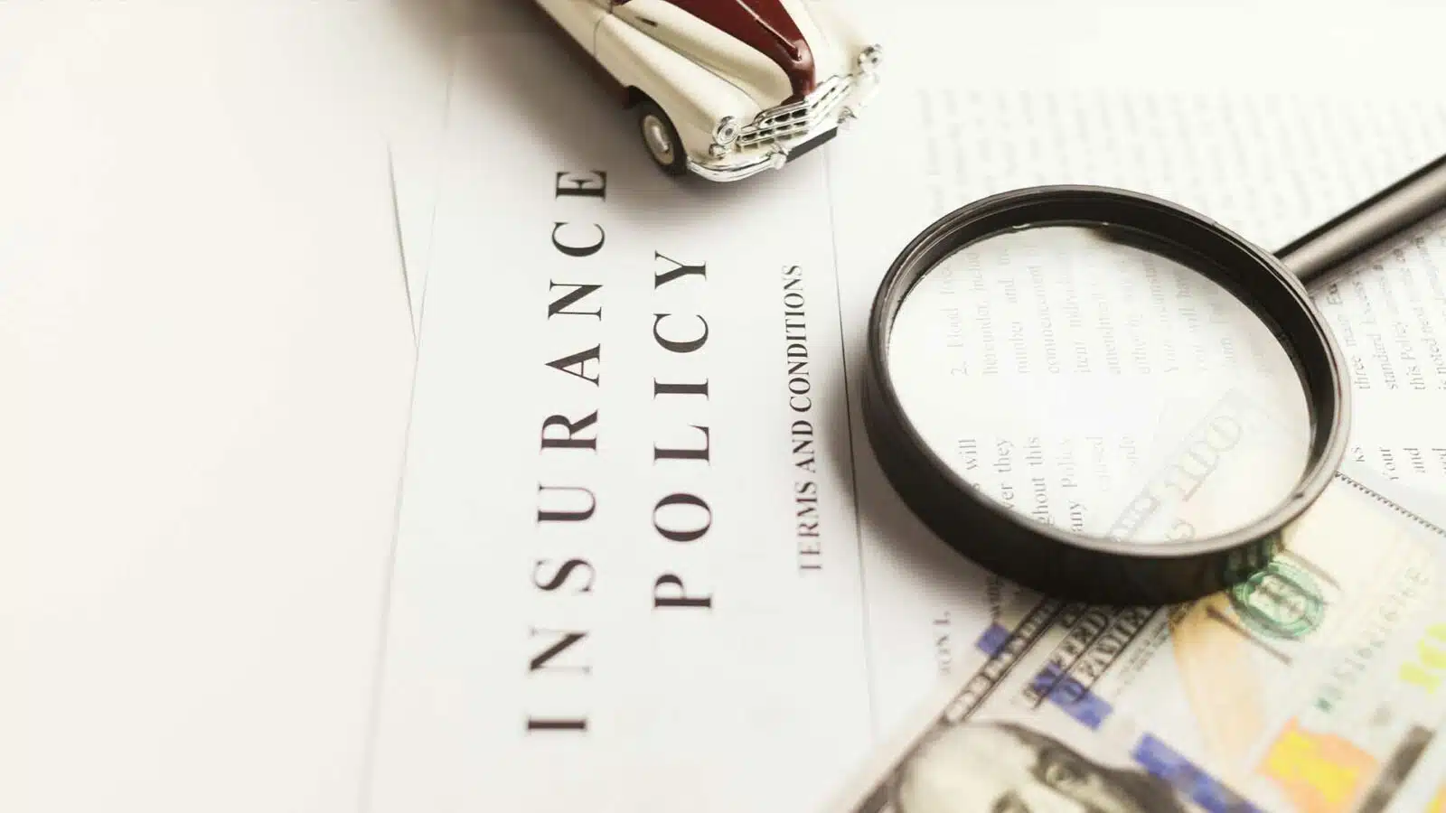 Car insurance policy document with money and magnifying glass.
