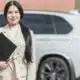 Professional woman with folder beside white car.