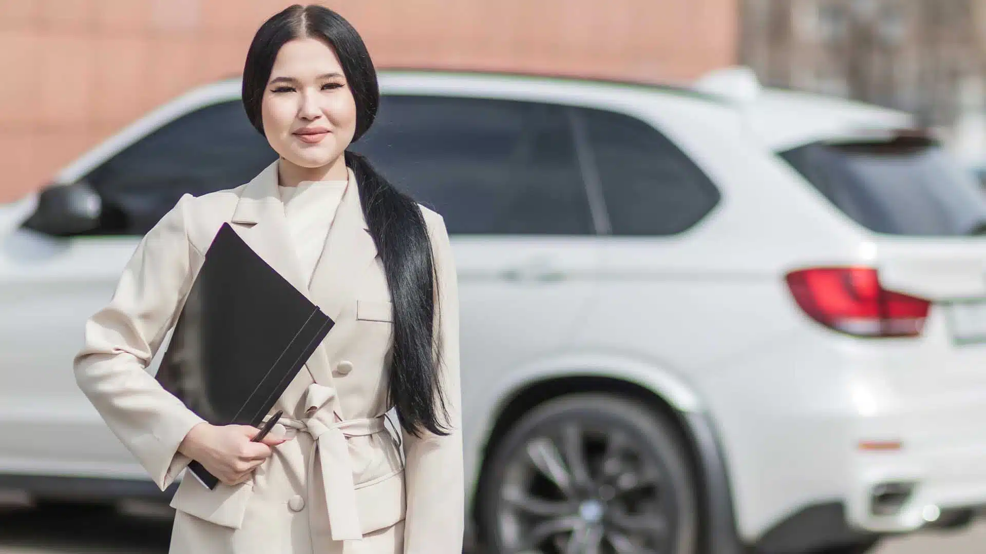Professional woman with folder beside white car.