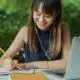 woman writing on notepad with a laptop next to her.